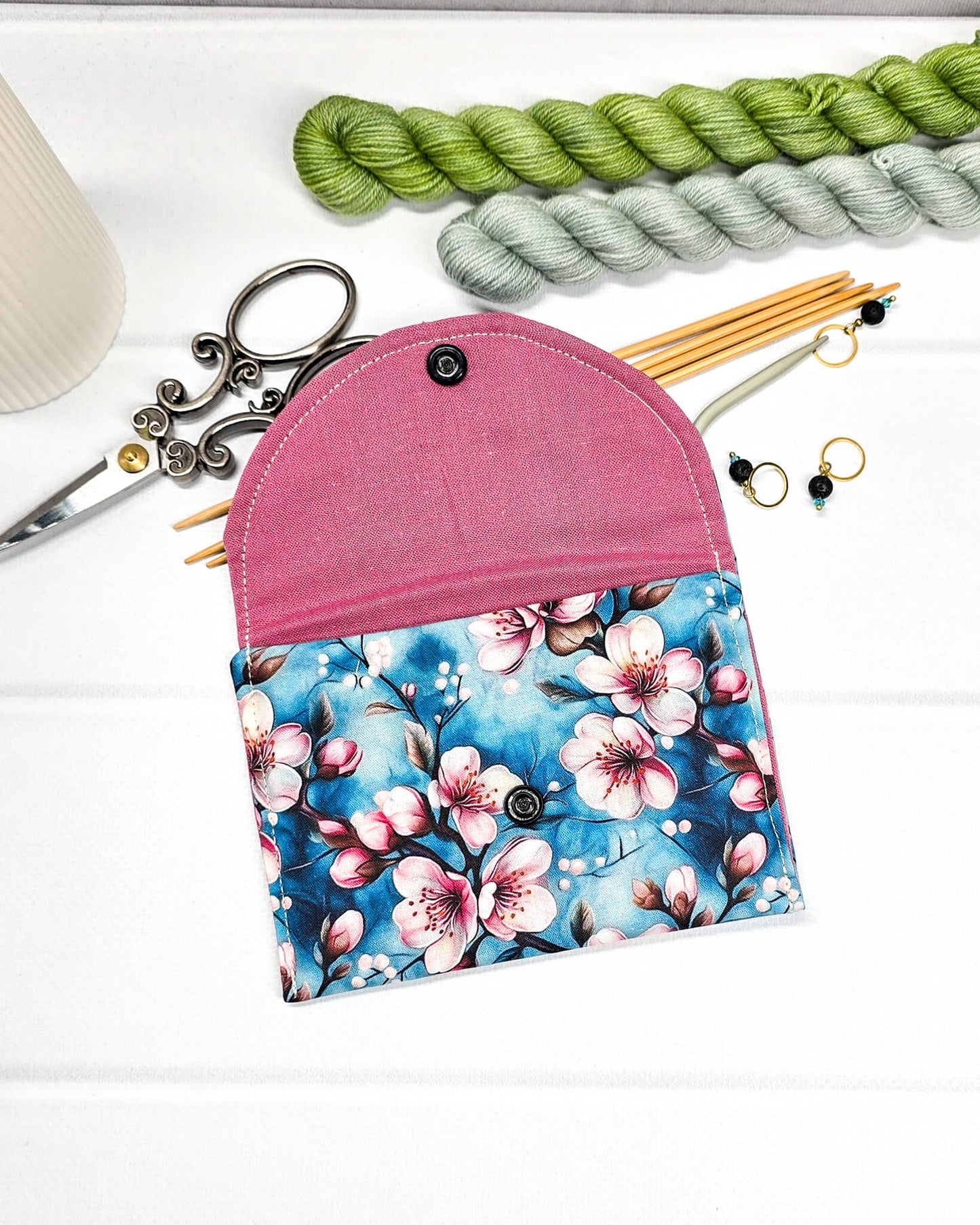 Kleine Mini Pouch mit rosa Kirschblütenmotiv auf blauem Grund und einem schwarzen Druckknopf. Handgenäht in Bayern von Nadelmikado.