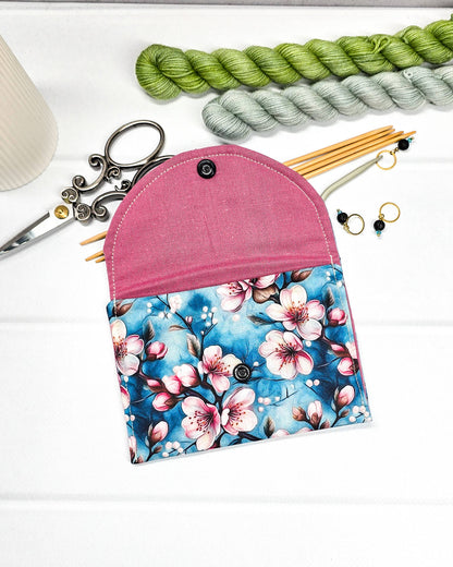 Kleine Mini Pouch mit rosa Kirschblütenmotiv auf blauem Grund und einem schwarzen Druckknopf. Handgenäht in Bayern von Nadelmikado.