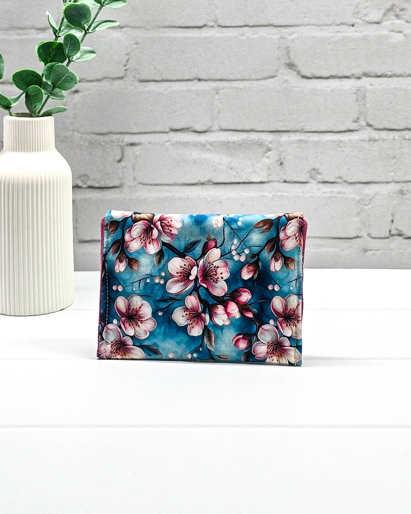 Kleine Mini Pouch mit rosa Kirschblütenmotiv auf blauem Grund und einem schwarzen Druckknopf. Handgenäht in Bayern von Nadelmikado.