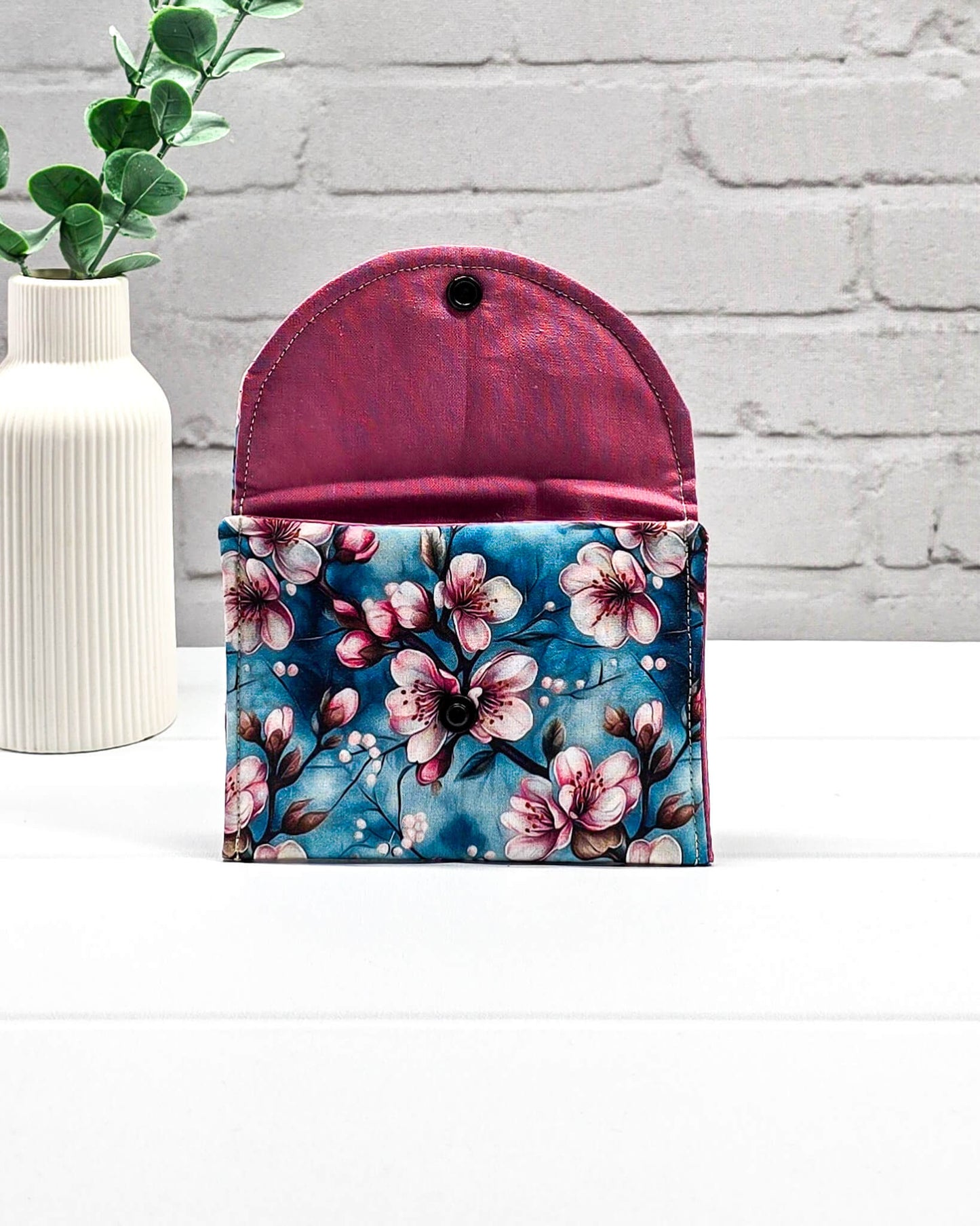 Kleine Mini Pouch mit rosa Kirschblütenmotiv auf blauem Grund und einem schwarzen Druckknopf. Handgenäht in Bayern von Nadelmikado.