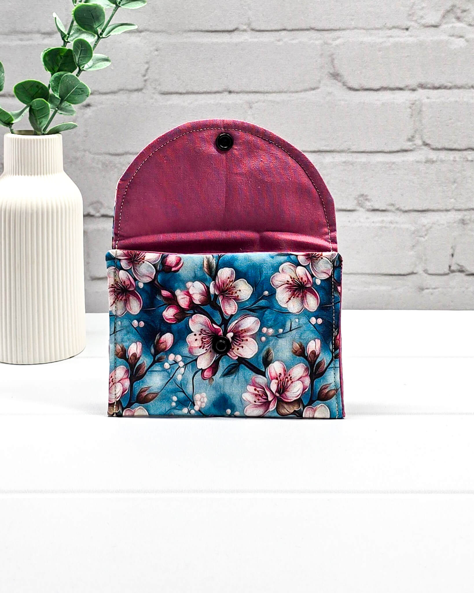 Kleine Mini Pouch mit rosa Kirschblütenmotiv auf blauem Grund und einem schwarzen Druckknopf. Handgenäht in Bayern von Nadelmikado.