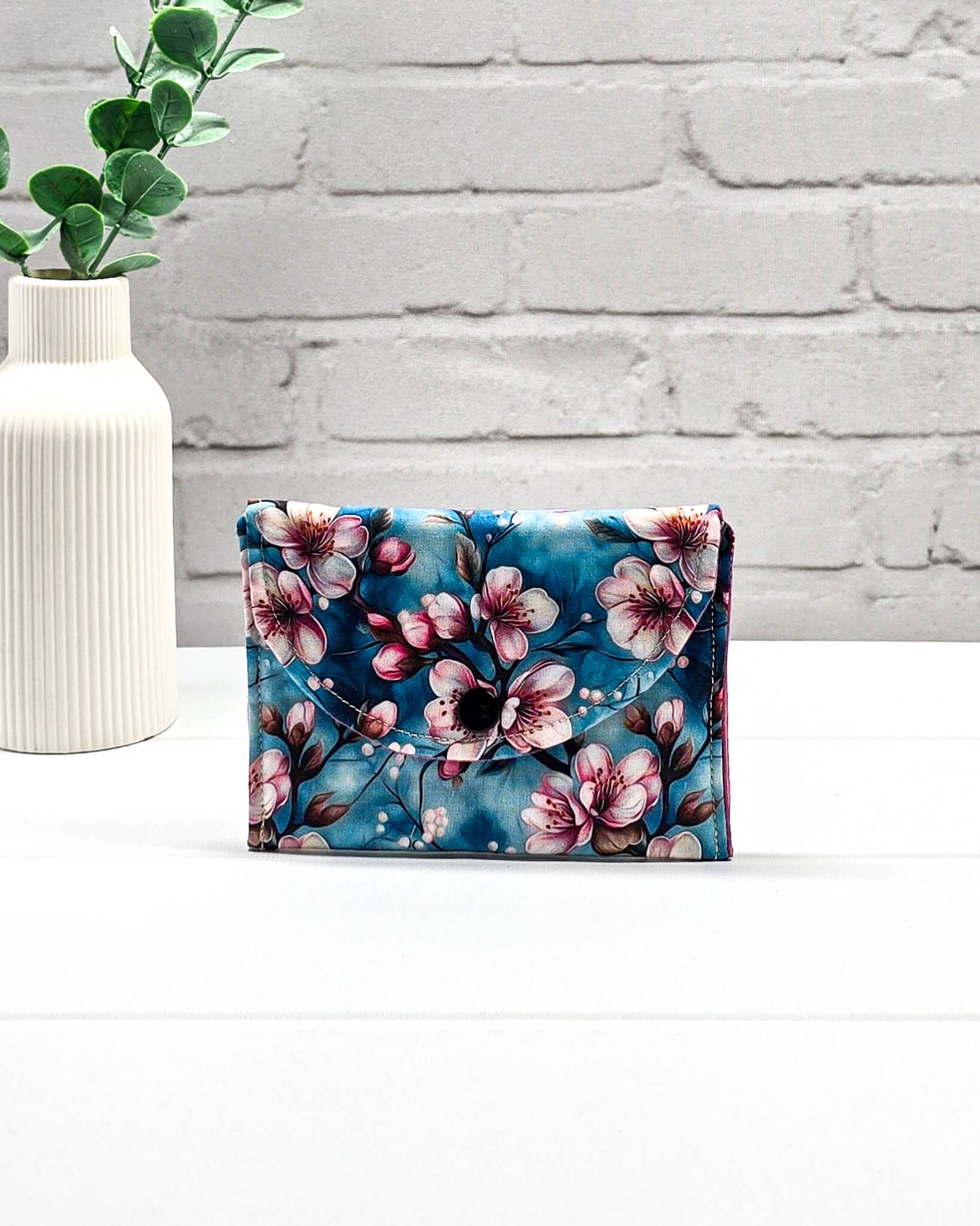 Kleine Mini Pouch mit rosa Kirschblütenmotiv auf blauem Grund und einem schwarzen Druckknopf. Handgenäht in Bayern von Nadelmikado.