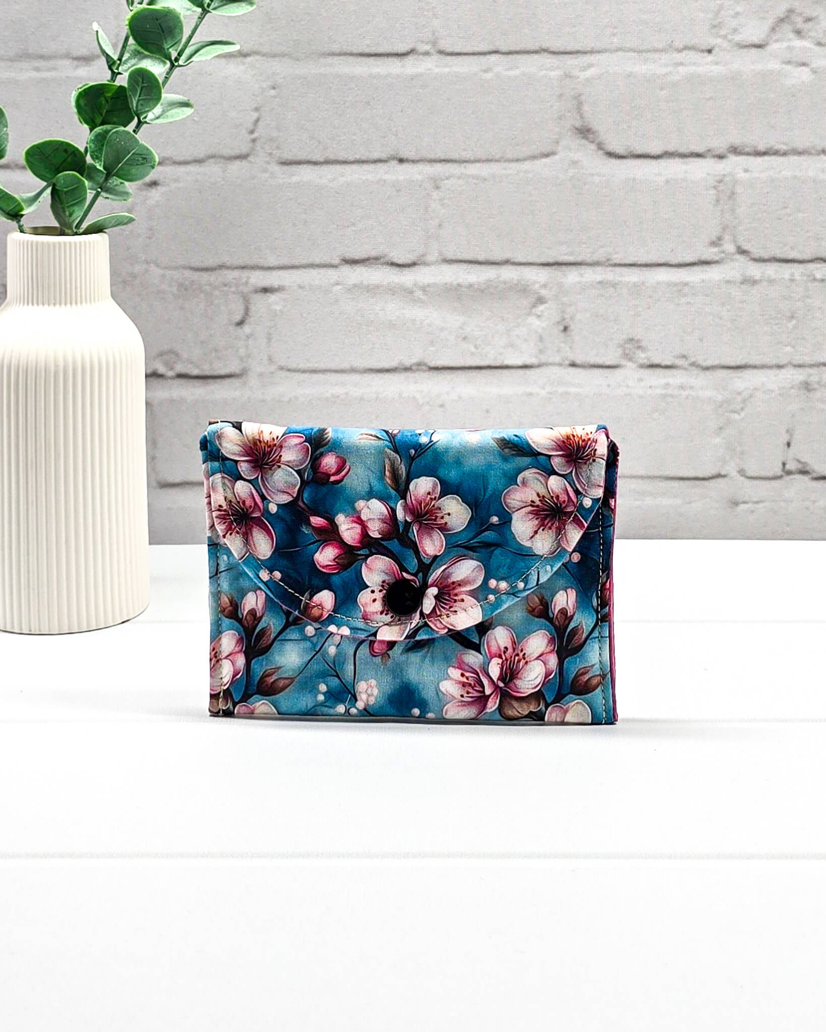Kleine Mini Pouch mit rosa Kirschblütenmotiv auf blauem Grund und einem schwarzen Druckknopf. Handgenäht in Bayern von Nadelmikado.