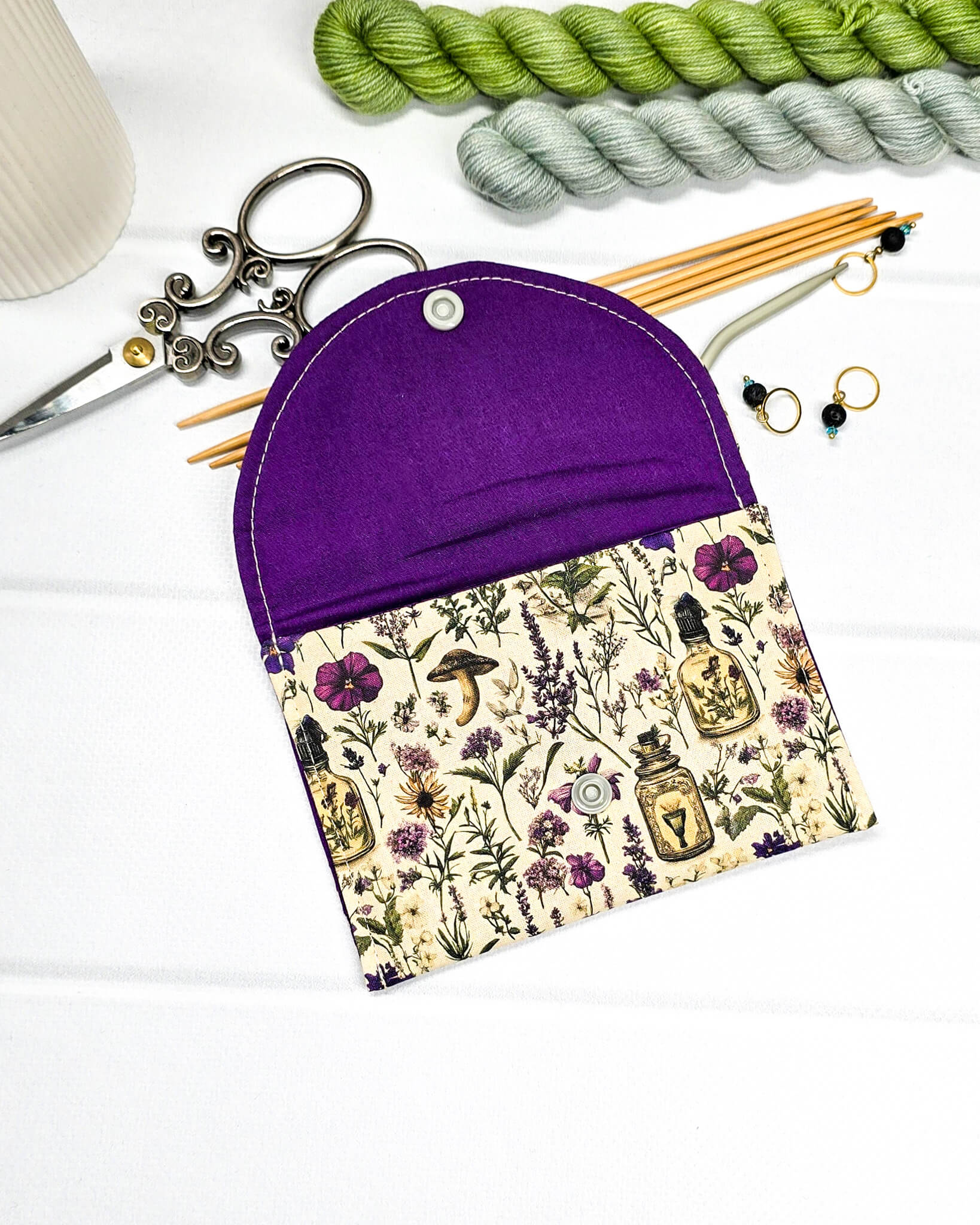 Kleine flache Zubehörtasche Mini Pouch mit abgerundeter Klappe, hellem Druckknopf und botanischem Kräuterküche-Muster auf beigem Grund. Handgenäht in Bayern von Nadelmikado.