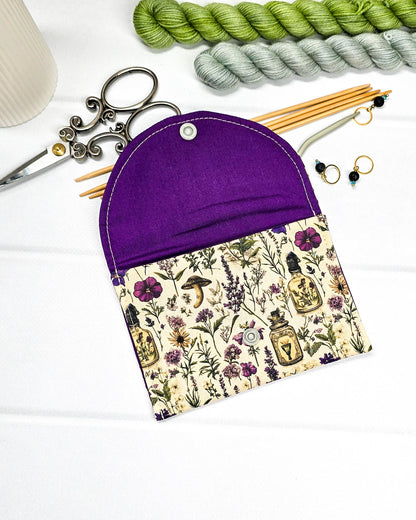 Kleine flache Zubehörtasche Mini Pouch mit abgerundeter Klappe, hellem Druckknopf und botanischem Kräuterküche-Muster auf beigem Grund. Handgenäht in Bayern von Nadelmikado.