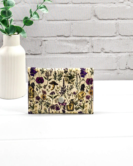 Kleine flache Zubehörtasche Mini Pouch mit abgerundeter Klappe, hellem Druckknopf und botanischem Kräuterküche-Muster auf beigem Grund. Handgenäht in Bayern von Nadelmikado.