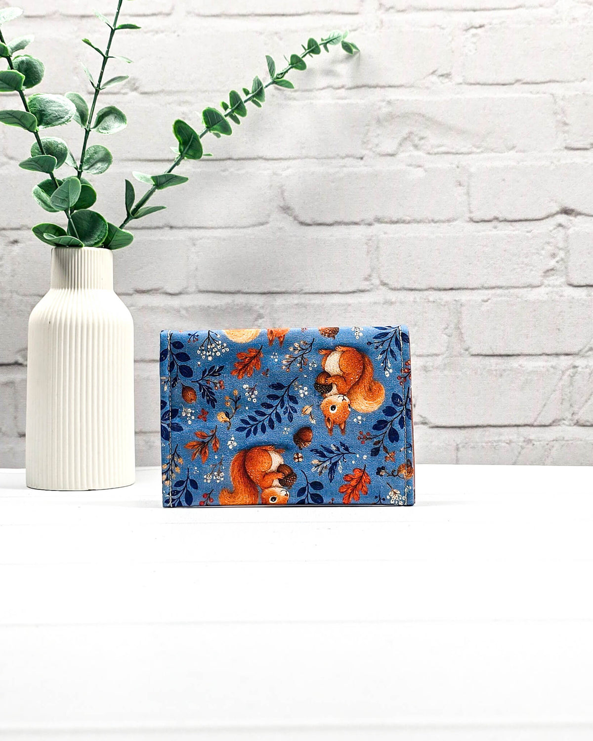 Mini Pouch für Strickzubehör aus blauem Baumwollstoff mit orangefarbenen Eichhörnchen und Eicheln, orangefarbener Klappe und Druckknopf. Handgenäht in Bayern von Nadelmikado.