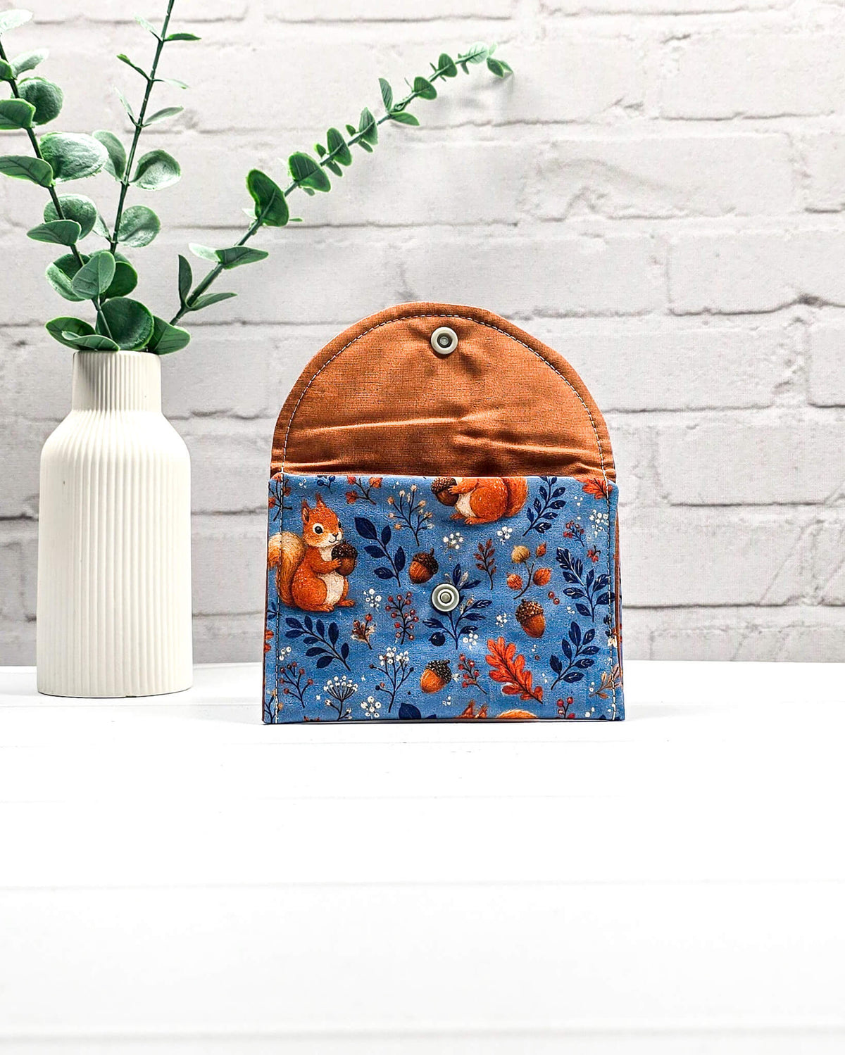 Mini Pouch für Strickzubehör aus blauem Baumwollstoff mit orangefarbenen Eichhörnchen und Eicheln, orangefarbener Klappe und Druckknopf. Handgenäht in Bayern von Nadelmikado.