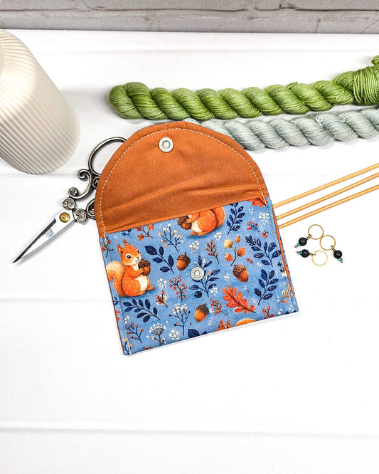 Mini Pouch für Strickzubehör aus blauem Baumwollstoff mit orangefarbenen Eichhörnchen und Eicheln, orangefarbener Klappe und Druckknopf. Handgenäht in Bayern von Nadelmikado.