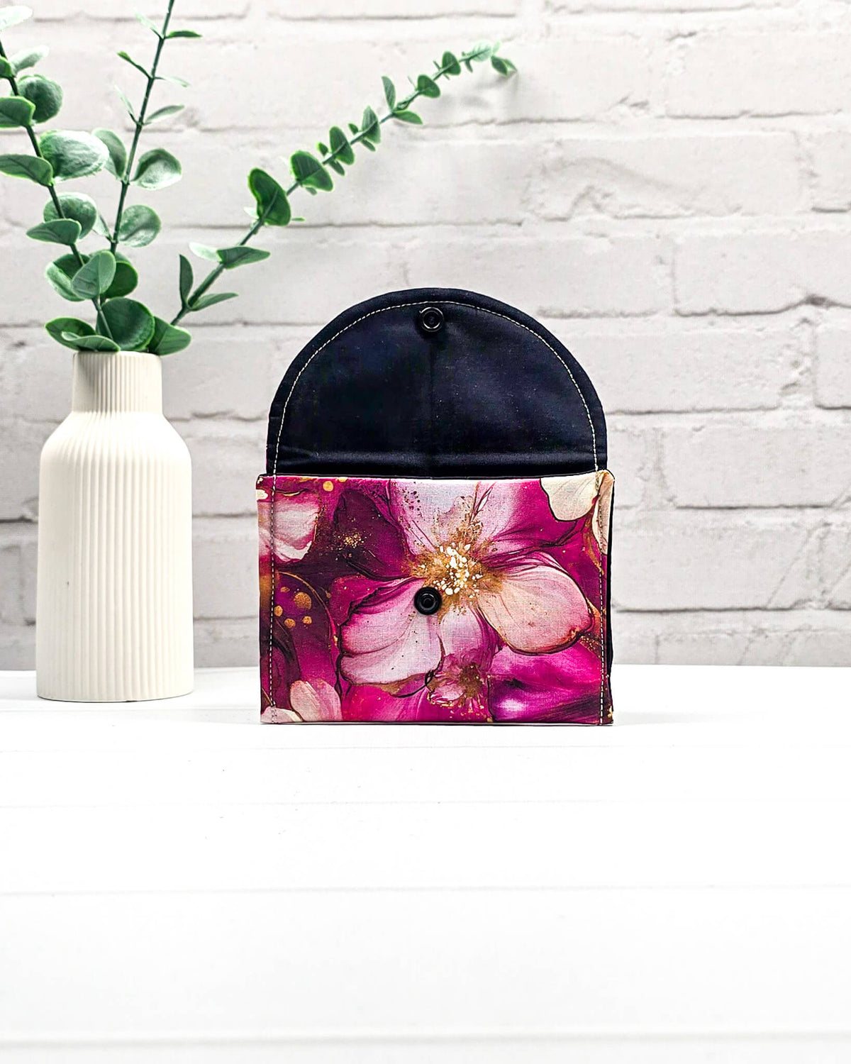 Geöffnete Mini Pouch mit großen pink-rosafarbenen Blüten und goldenen Akzenten, schwarzer Innenklappe und Druckknopfverschluss. Kleine Zubehörtasche für Maschenmarkierer und Strickzubehör. Handgenäht in Bayern von NadelMikado.