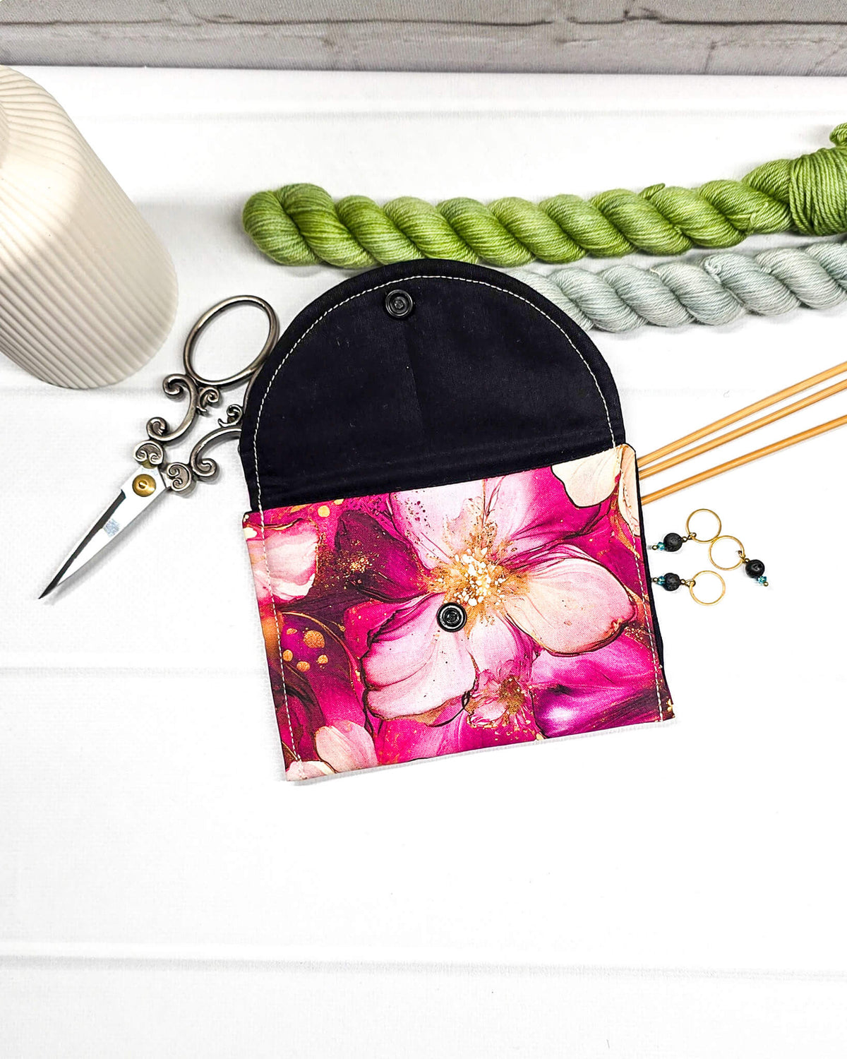 Geöffnete Mini Pouch mit großen pink-rosafarbenen Blüten und goldenen Akzenten, schwarzer Innenklappe und Druckknopfverschluss. Kleine Zubehörtasche für Maschenmarkierer und Strickzubehör. Handgenäht in Bayern von NadelMikado.