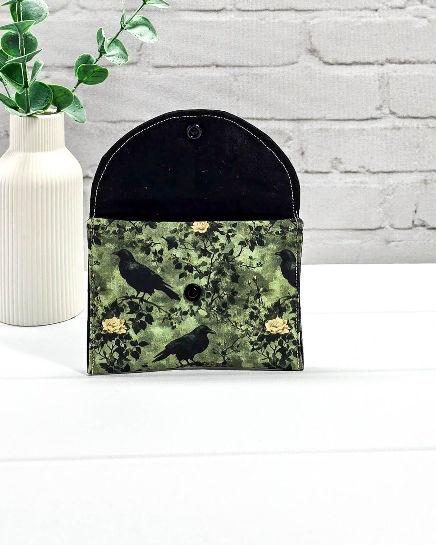 Kleine grüne Zubehörtasche mit Druckknopf, gemustert mit Raben und Rosen, genutzt als Mini Pouch für Maschenmarkierer und Strickzubehör. Handgenäht von Nadelmikado.
