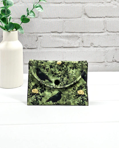 Kleine grüne Zubehörtasche mit Druckknopf, gemustert mit Raben und Rosen, genutzt als Mini Pouch für Maschenmarkierer und Strickzubehör. Handgenäht von Nadelmikado.