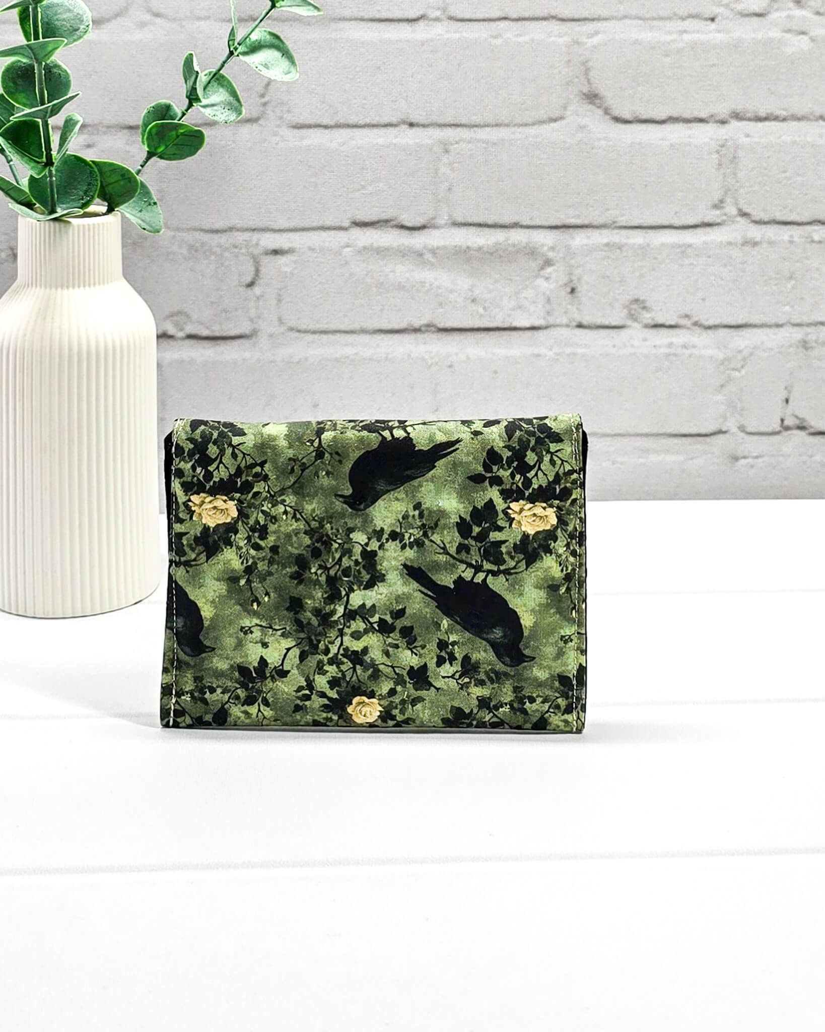 Kleine grüne Zubehörtasche mit Druckknopf, gemustert mit Raben und Rosen, genutzt als Mini Pouch für Maschenmarkierer und Strickzubehör. Handgenäht von Nadelmikado.