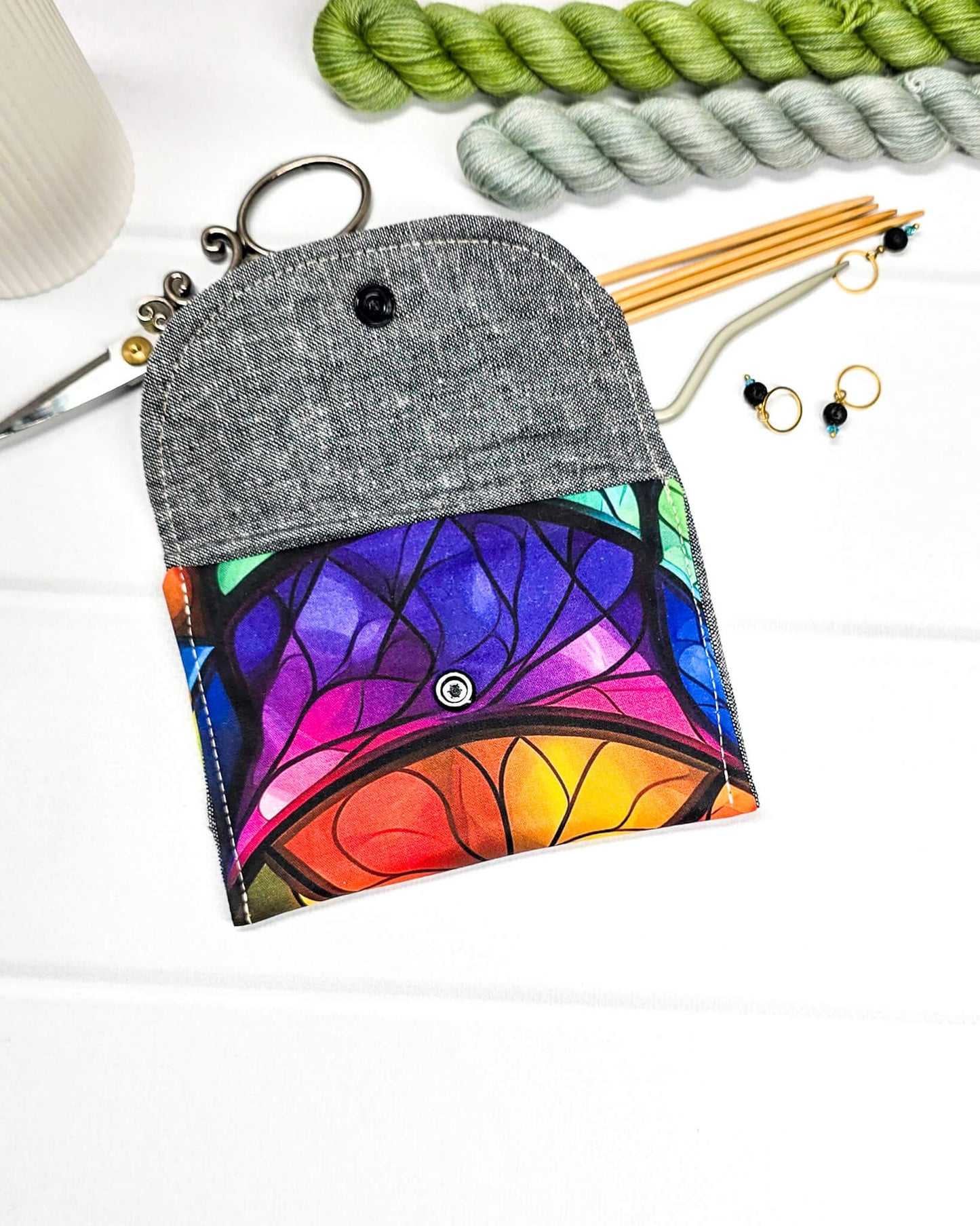 Mini Pouch mit einem farbenfrohen Regenbogen-Muster im Kirchenglas-Stil, geschwungener Klappe und einem schwarzen Druckknopf. Handgenäht in Bayern von Nadelmikado. 