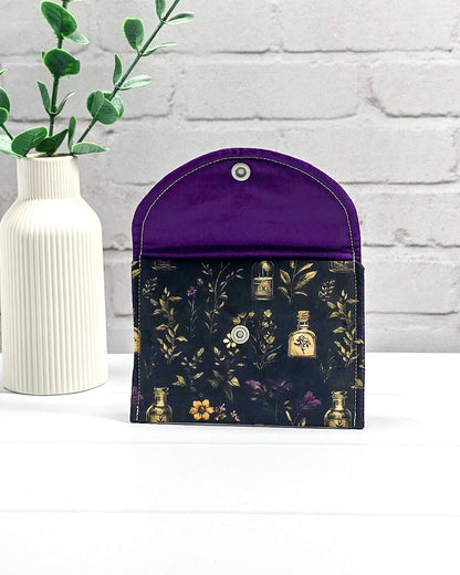 Mini Pouch Secret Garden für Strickzubehör mit dunklem botanischem Muster, goldenen Fläschchen und violettem Innenfutter. Handgenäht in Bayern von NadelMikado.