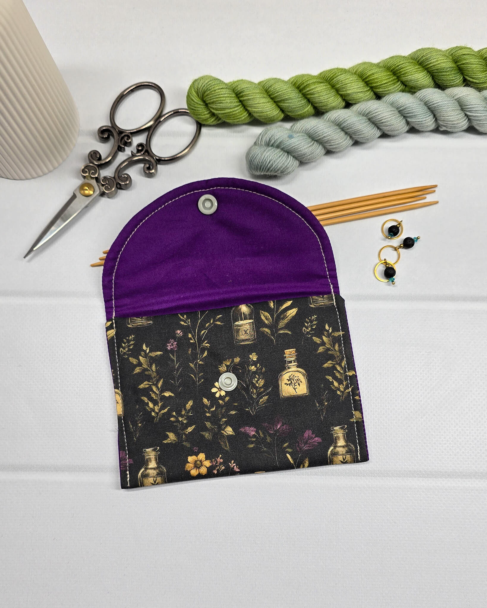 Mini Pouch Secret Garden für Strickzubehör mit dunklem botanischem Muster, goldenen Fläschchen und violettem Innenfutter. Handgenäht in Bayern von NadelMikado.