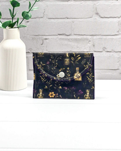 Mini Pouch Secret Garden für Strickzubehör mit dunklem botanischem Muster, goldenen Fläschchen und violettem Innenfutter. Handgenäht in Bayern von NadelMikado.