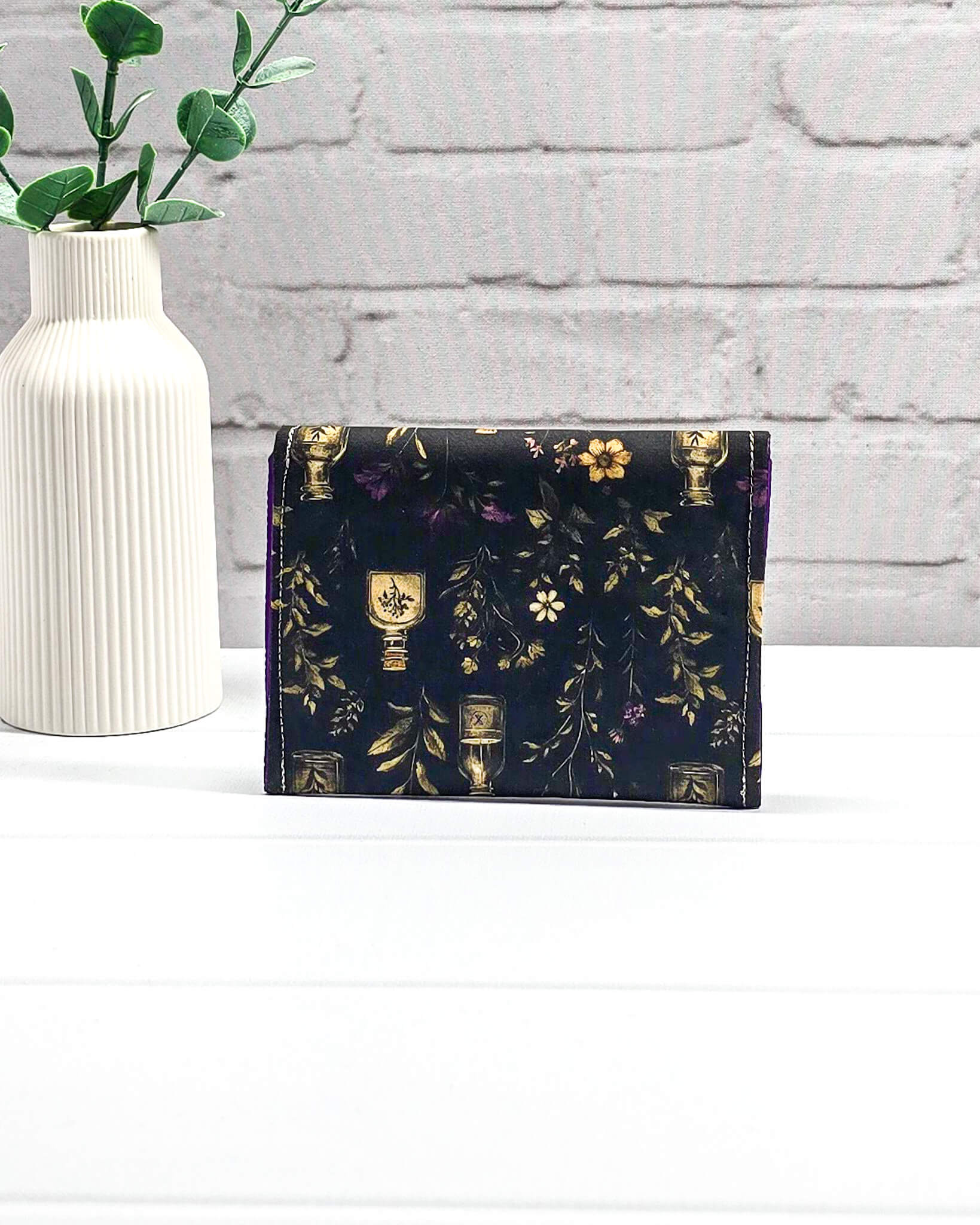 Mini Pouch Secret Garden für Strickzubehör mit dunklem botanischem Muster, goldenen Fläschchen und violettem Innenfutter. Handgenäht in Bayern von NadelMikado.