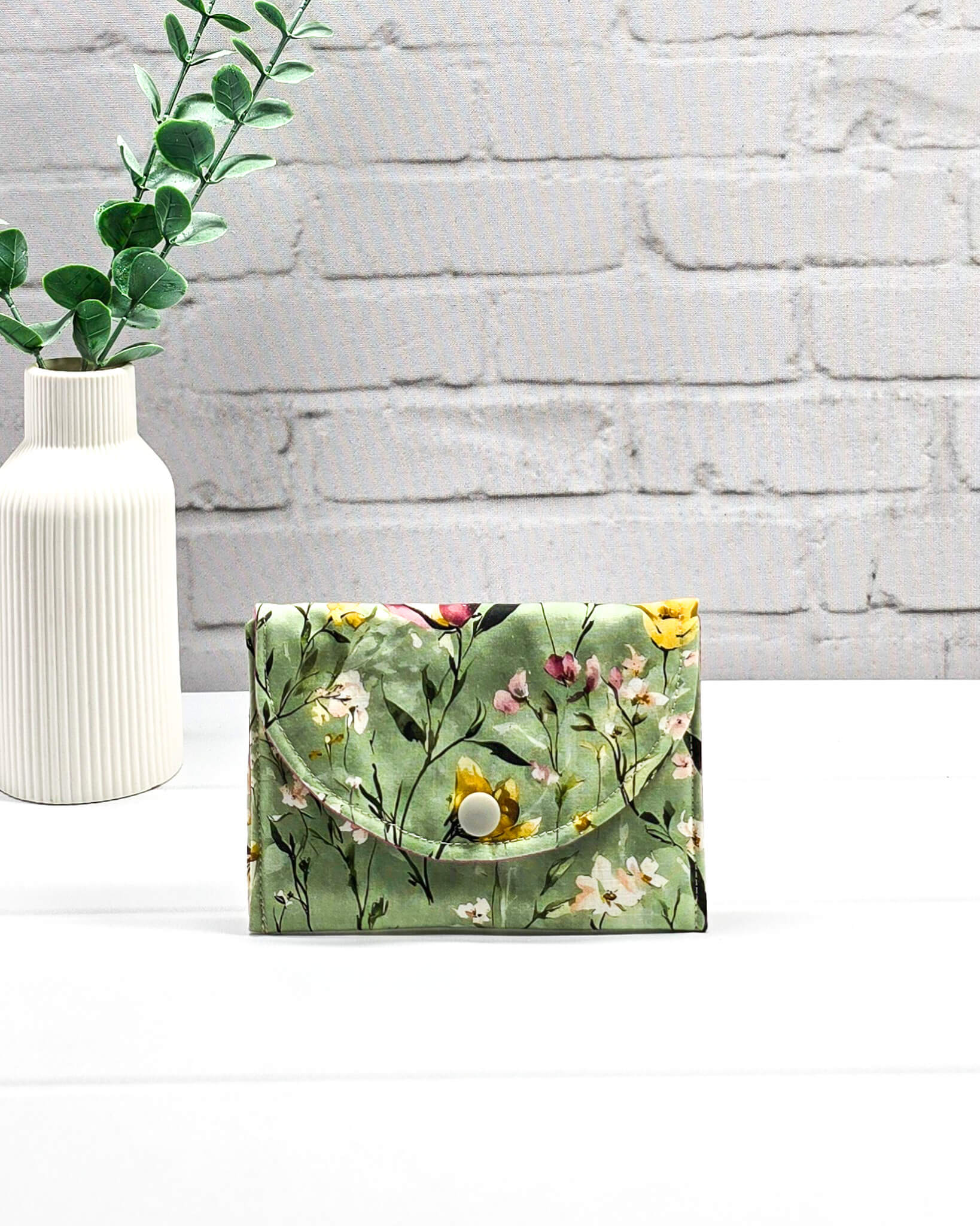 Kleine Mini Pouch mit buntem Wildblumenmotiv auf salbeigrünem Grund und einem hellgrauen Druckknopf. Handgenäht in Bayern von Nadelmikado.