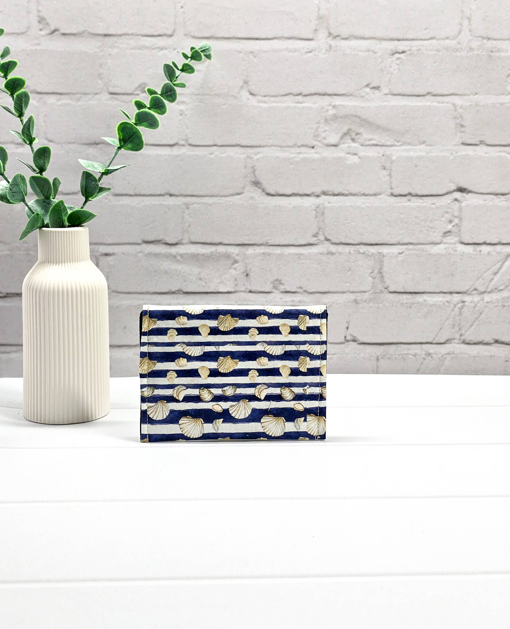 Kleine Mini Pouch aus blau-weiß quergestreiftem Stoff mit kleinen Muschelmotiven und einem hellgrauen Druckknopf auf der geschwungenen Klappe. Handgenäht in Bayern von Nadelmikado. 