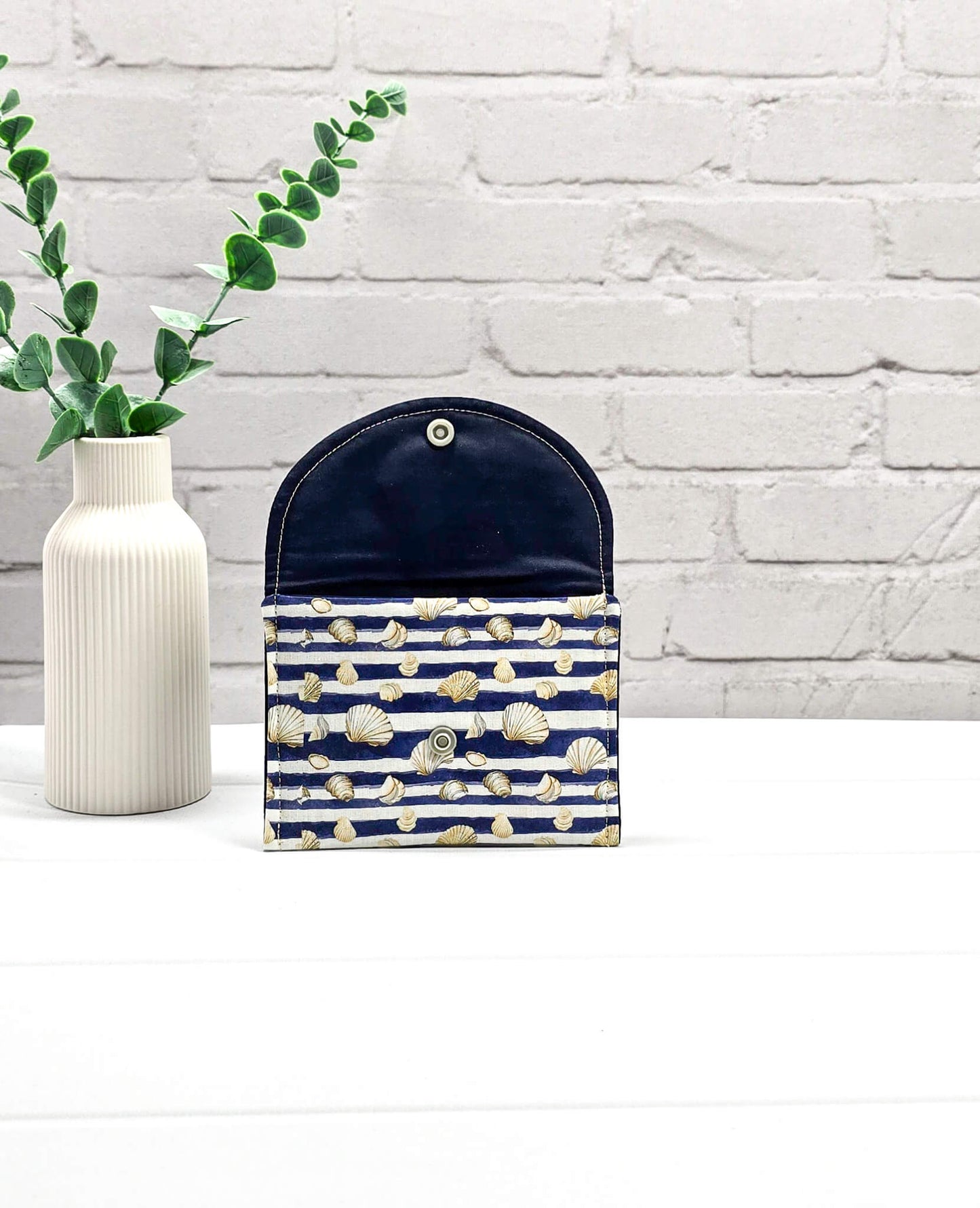 Kleine Mini Pouch aus blau-weiß quergestreiftem Stoff mit kleinen Muschelmotiven und einem hellgrauen Druckknopf auf der geschwungenen Klappe. Handgenäht in Bayern von Nadelmikado. 