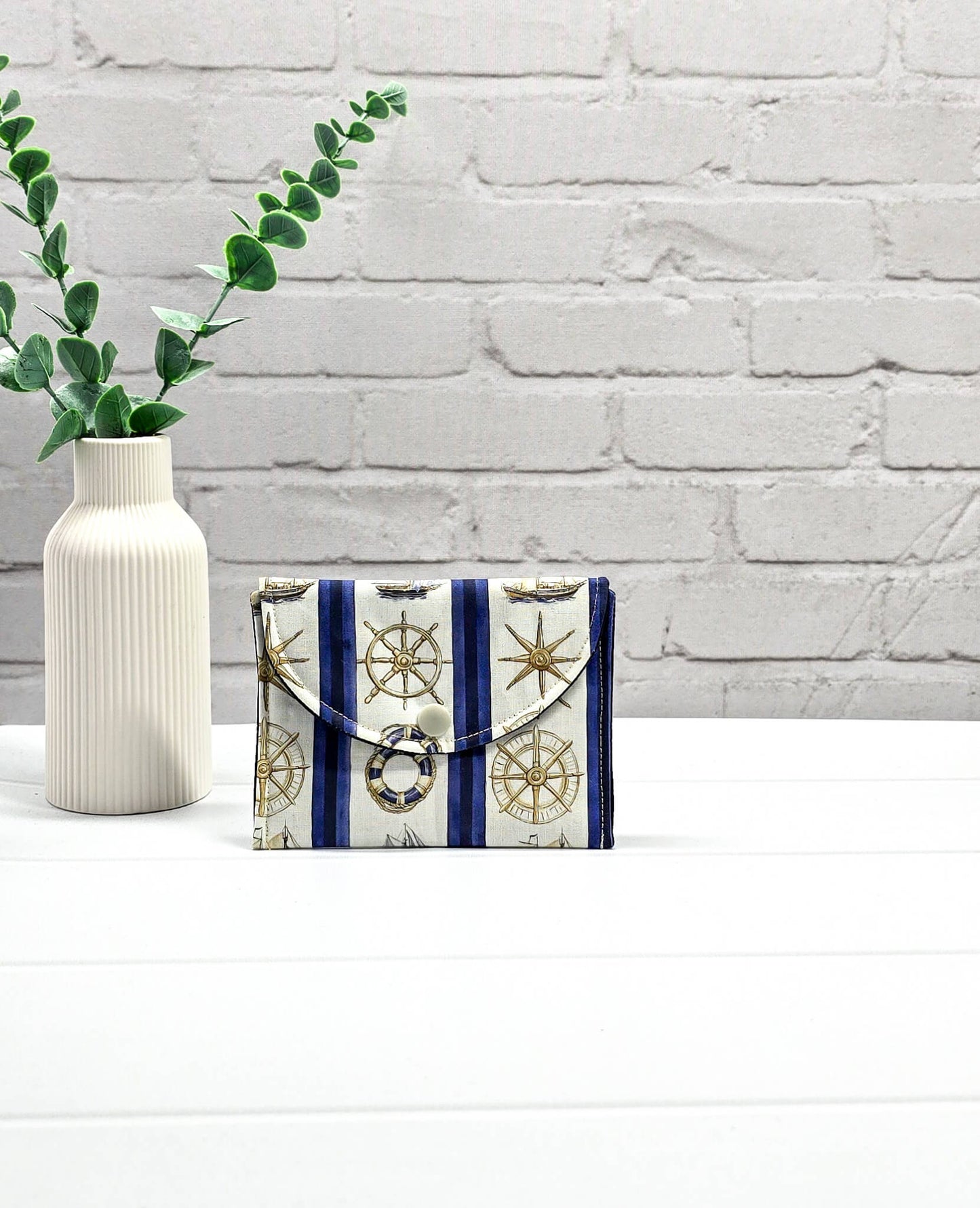 Kleine Mini Pouch aus cremeweißem Stoff mit blauen Längsstreifen, maritimen Motiven und einem hellen Druckknopf auf der geschwungenen Klappe. Handgenäht in Bayern von Nadelmikado. 