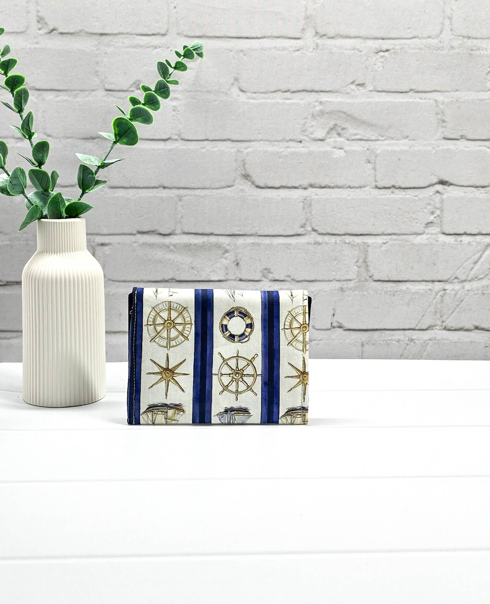 Kleine Mini Pouch aus cremeweißem Stoff mit blauen Längsstreifen, maritimen Motiven und einem hellen Druckknopf auf der geschwungenen Klappe. Handgenäht in Bayern von Nadelmikado. 