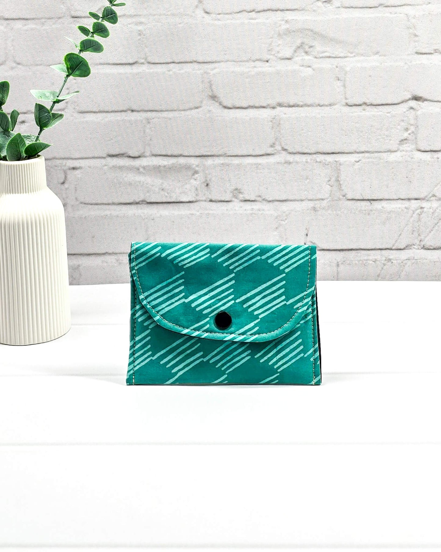 Kleine, flache Mini-Pouch für Strickzubehör mit hellem, grafischem Linienmuster auf smaragdgrünem Stoff, verschlossen mit einer Klappe und einem schwarzen Druckknopf. Handgenäht in Bayern von Nadelmikado.