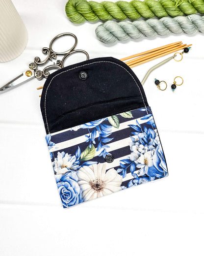 Kleine, flache Mini-Pouch für Handarbeitszubehör mit blauen Rosen und weißen Blüten auf blau-weiß gestreiftem Stoff, verschlossen mit einer Klappe und einem schwarzen Druckknopf. Handgenäht in Bayern von Nadelmikado