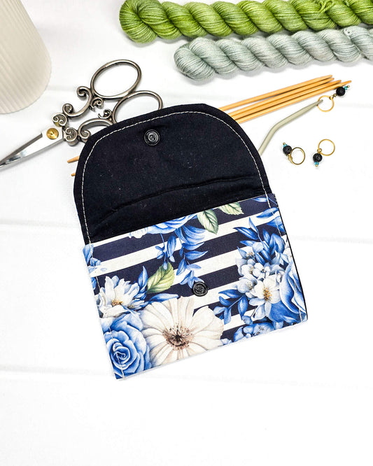 Kleine, flache Mini-Pouch für Handarbeitszubehör mit blauen Rosen und weißen Blüten auf blau-weiß gestreiftem Stoff, verschlossen mit einer Klappe und einem schwarzen Druckknopf. Handgenäht in Bayern von Nadelmikado