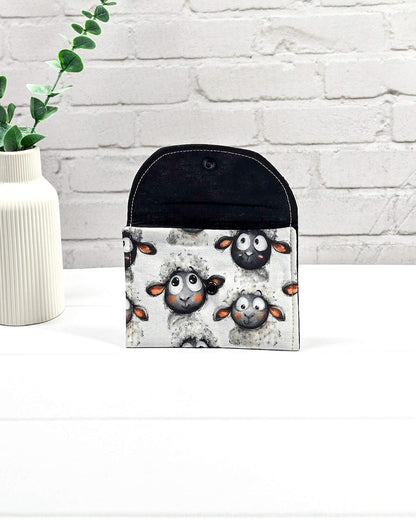 Kleine, flache Mini-Pouch für Handarbeitszubehör mit drolligem Schaf-Motiv auf hellgrau meliertem Stoff, verschlossen mit einer Klappe und einem schwarzen Druckknopf. Handgenäht in Bayern von Nadelmikado. 