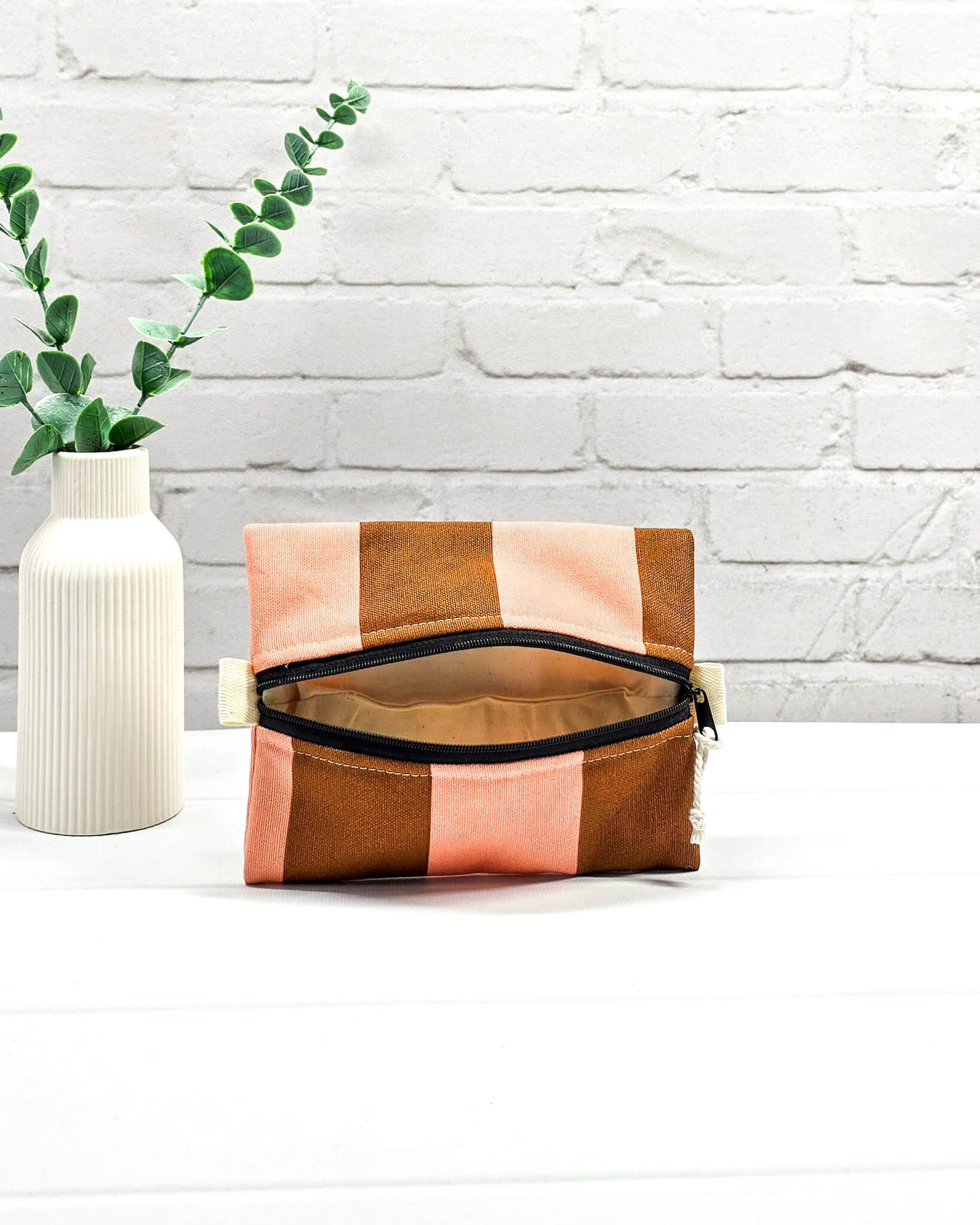 Mini Zip Pouch mit breiten vertikalen Streifen in Braun und Rosa, einem schwarzen, mittigen Reißverschluss und hellen Stofflaschen. Handgenäht in Bayern von Nadelmikado. 