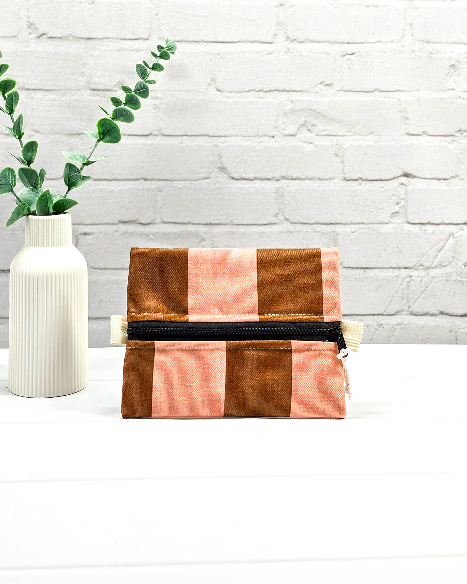 Mini Zip Pouch mit breiten vertikalen Streifen in Braun und Rosa, einem schwarzen, mittigen Reißverschluss und hellen Stofflaschen. Handgenäht in Bayern von Nadelmikado. 