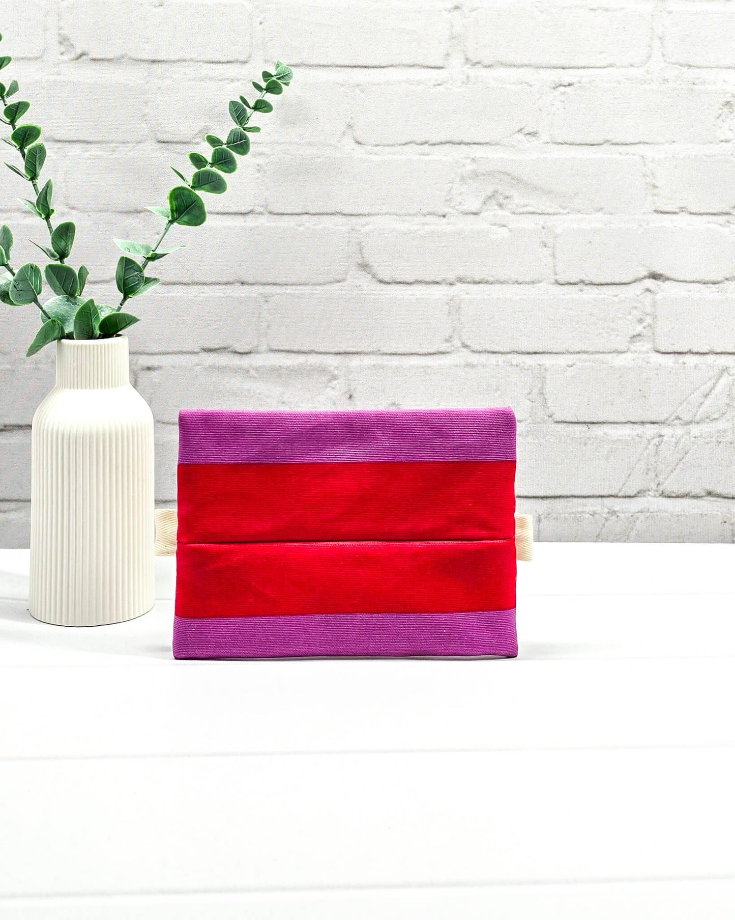 Mini Zip Pouch mit breiten horizontalen Streifen in Rot und Violett, einem schwarzen mittigen Reißverschluss und hellen Stofflaschen. Handgenäht in Bayern von Nadelmikado