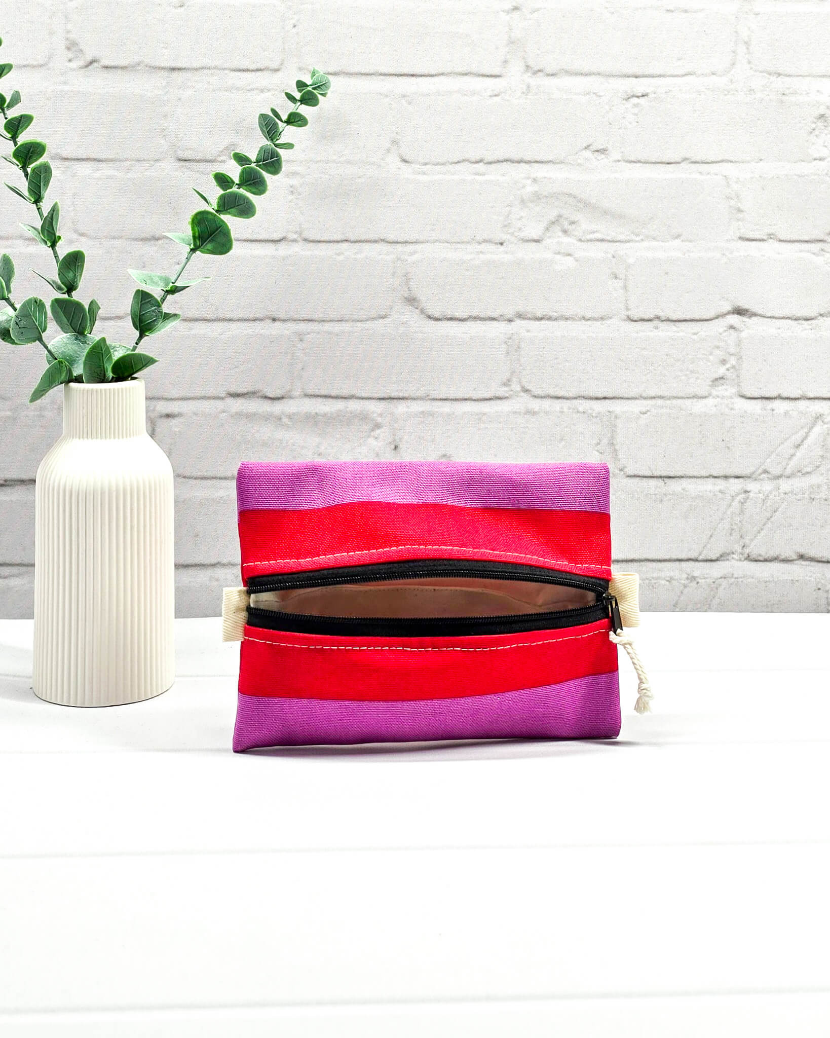Mini Zip Pouch mit breiten horizontalen Streifen in Rot und Violett, einem schwarzen mittigen Reißverschluss und hellen Stofflaschen. Handgenäht in Bayern von Nadelmikado
