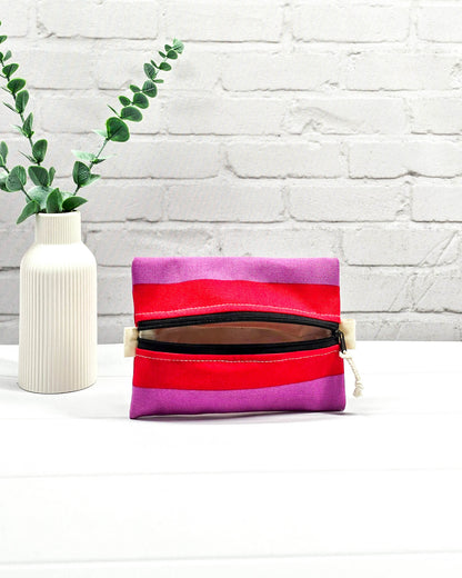 Mini Zip Pouch mit breiten horizontalen Streifen in Rot und Violett, einem schwarzen mittigen Reißverschluss und hellen Stofflaschen. Handgenäht in Bayern von Nadelmikado