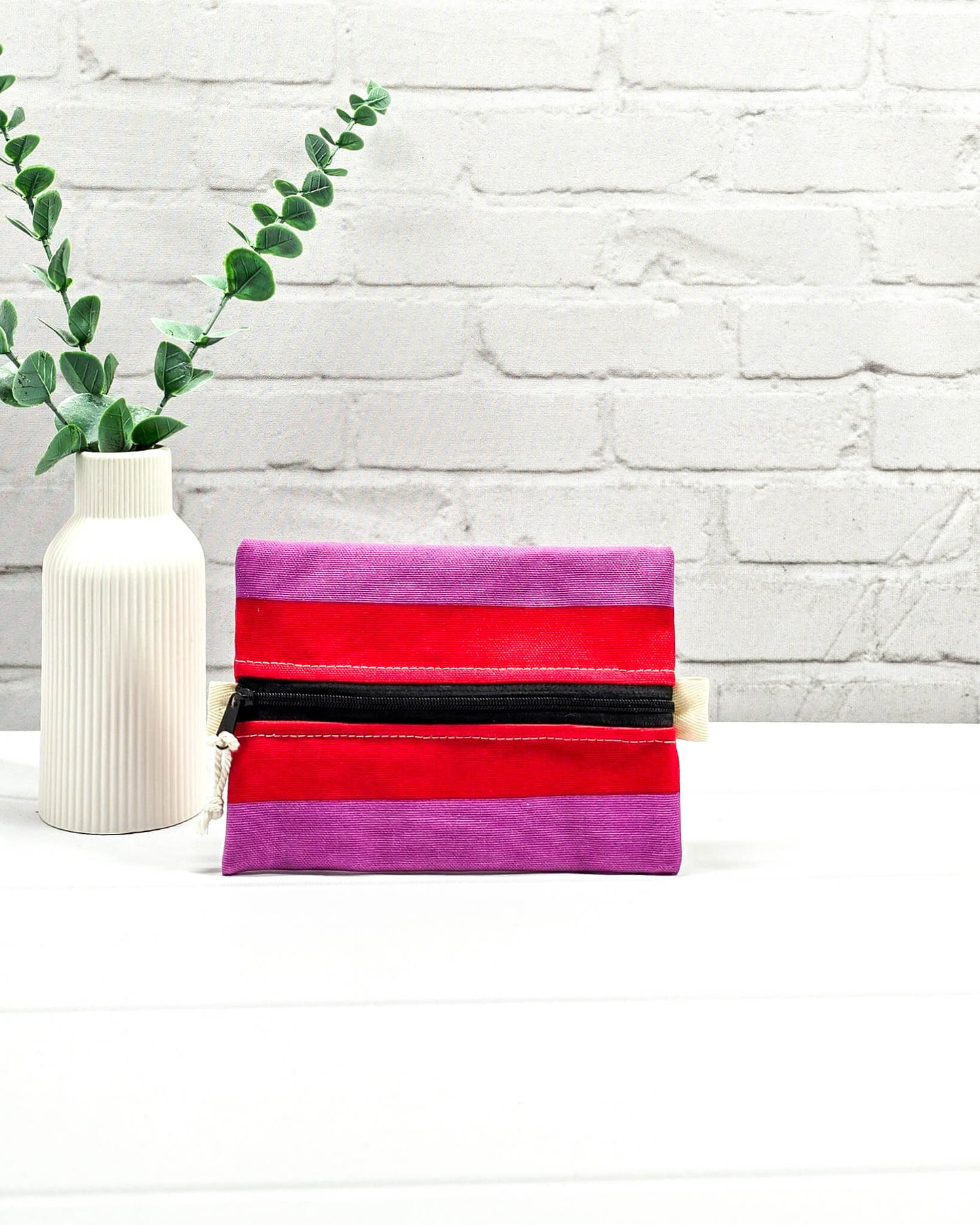 Mini Zip Pouch mit breiten horizontalen Streifen in Rot und Violett, einem schwarzen mittigen Reißverschluss und hellen Stofflaschen. Handgenäht in Bayern von Nadelmikado