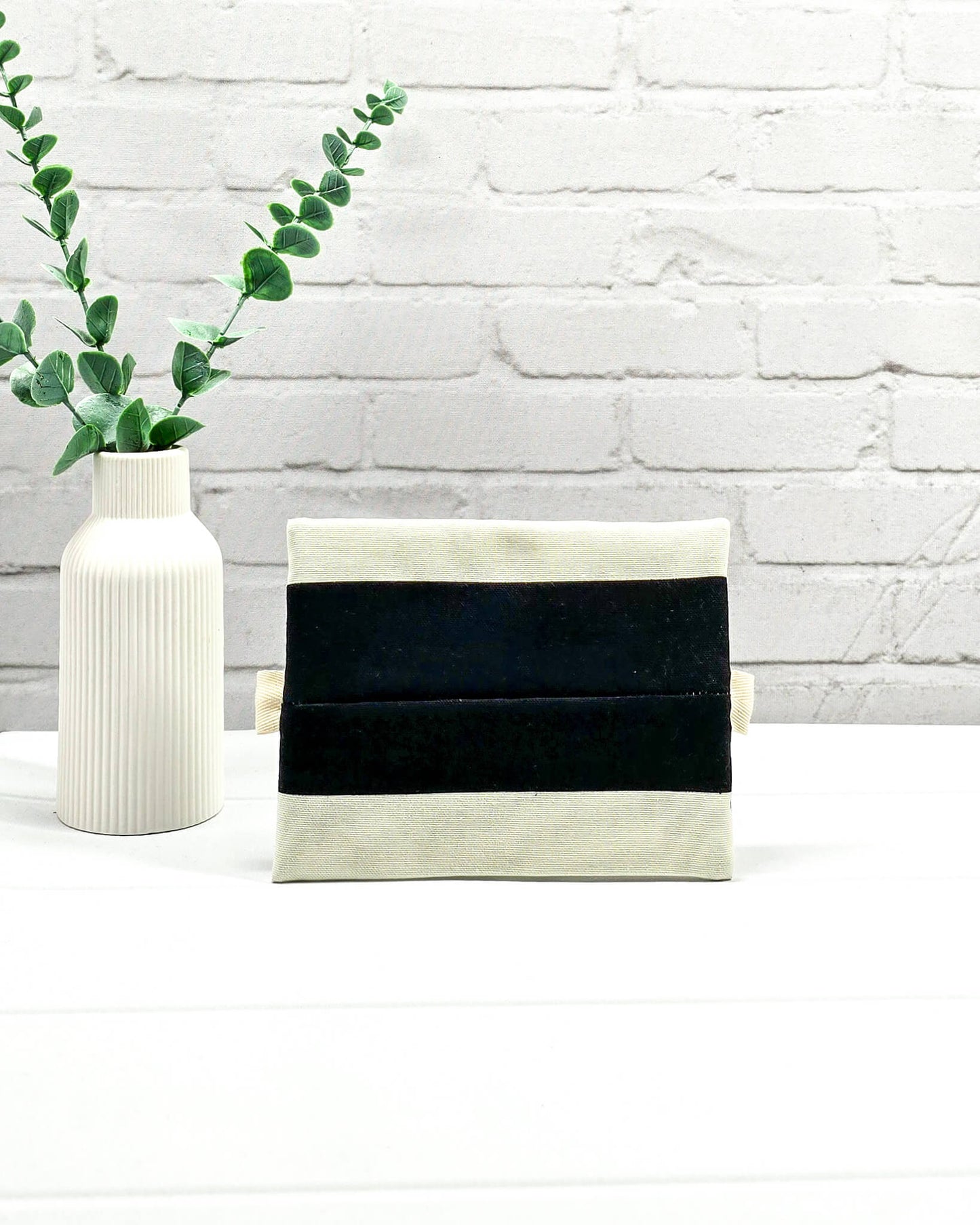 Mini Zip Pouch mit breiten horizontalen Streifen in Schwarz und Creme, einem schwarzen mittigen Reißverschluss und hellen Stofflaschen. Handgenäht in Bayern von Nadelmikado. 