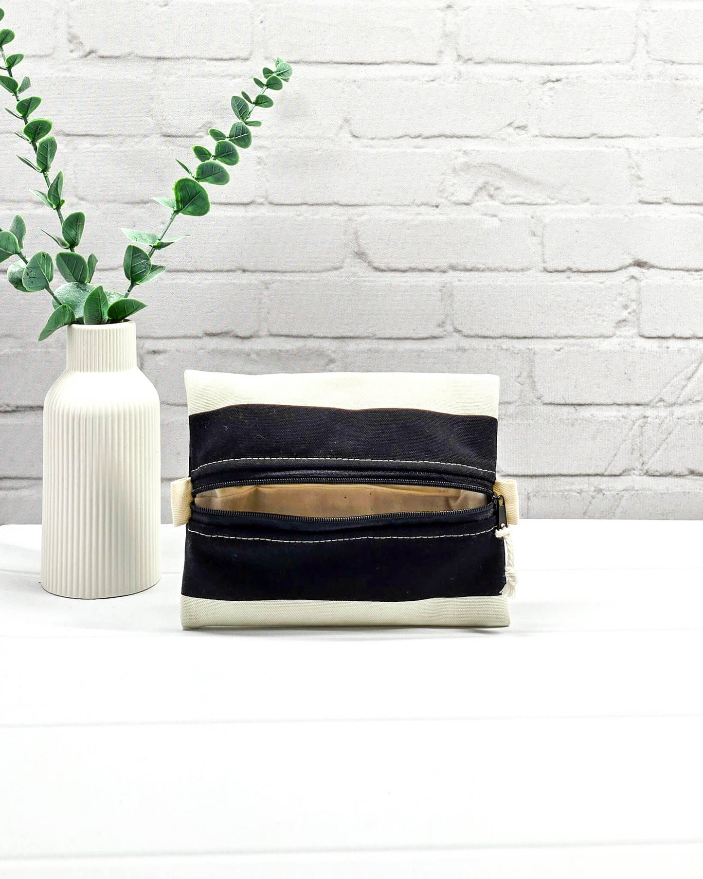 Mini Zip Pouch mit breiten horizontalen Streifen in Schwarz und Creme, einem schwarzen mittigen Reißverschluss und hellen Stofflaschen. Handgenäht in Bayern von Nadelmikado. 