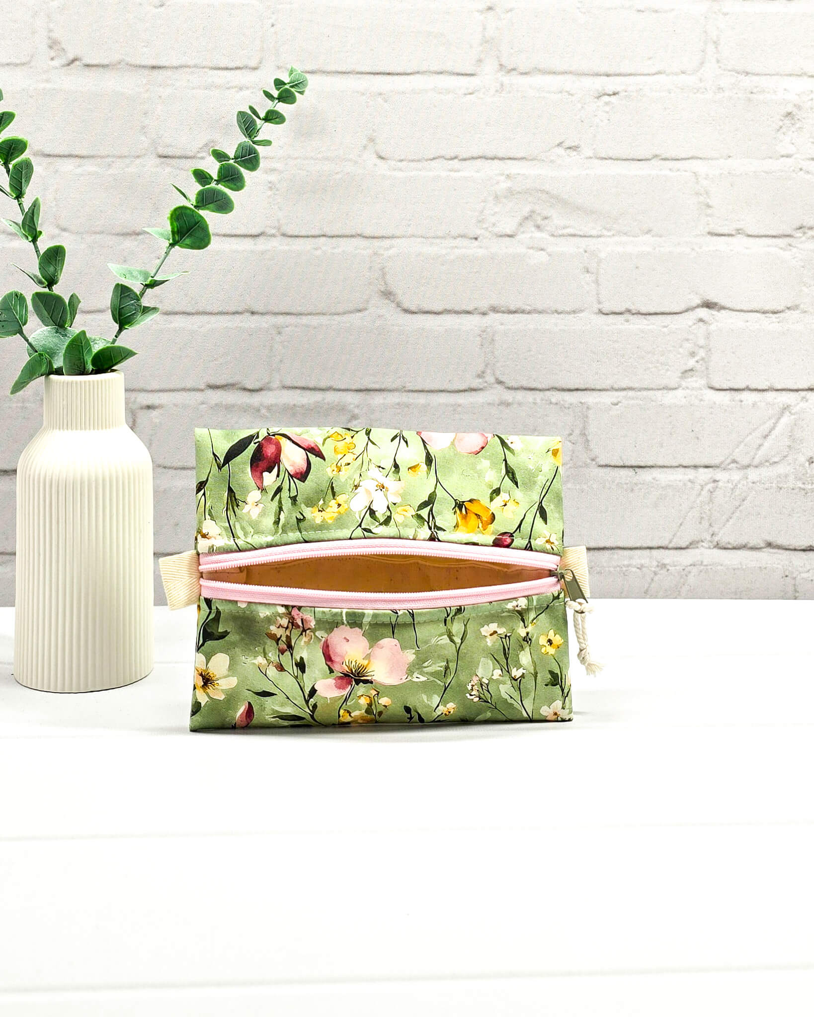 Mini Zip Pouch mit einem floralen Muster auf olivgrünem Stoff, einem rosafarbenen mittigen Reißverschluss und hellen Stofflaschen. Handgenäht in Bayern von Nadelmikado. 