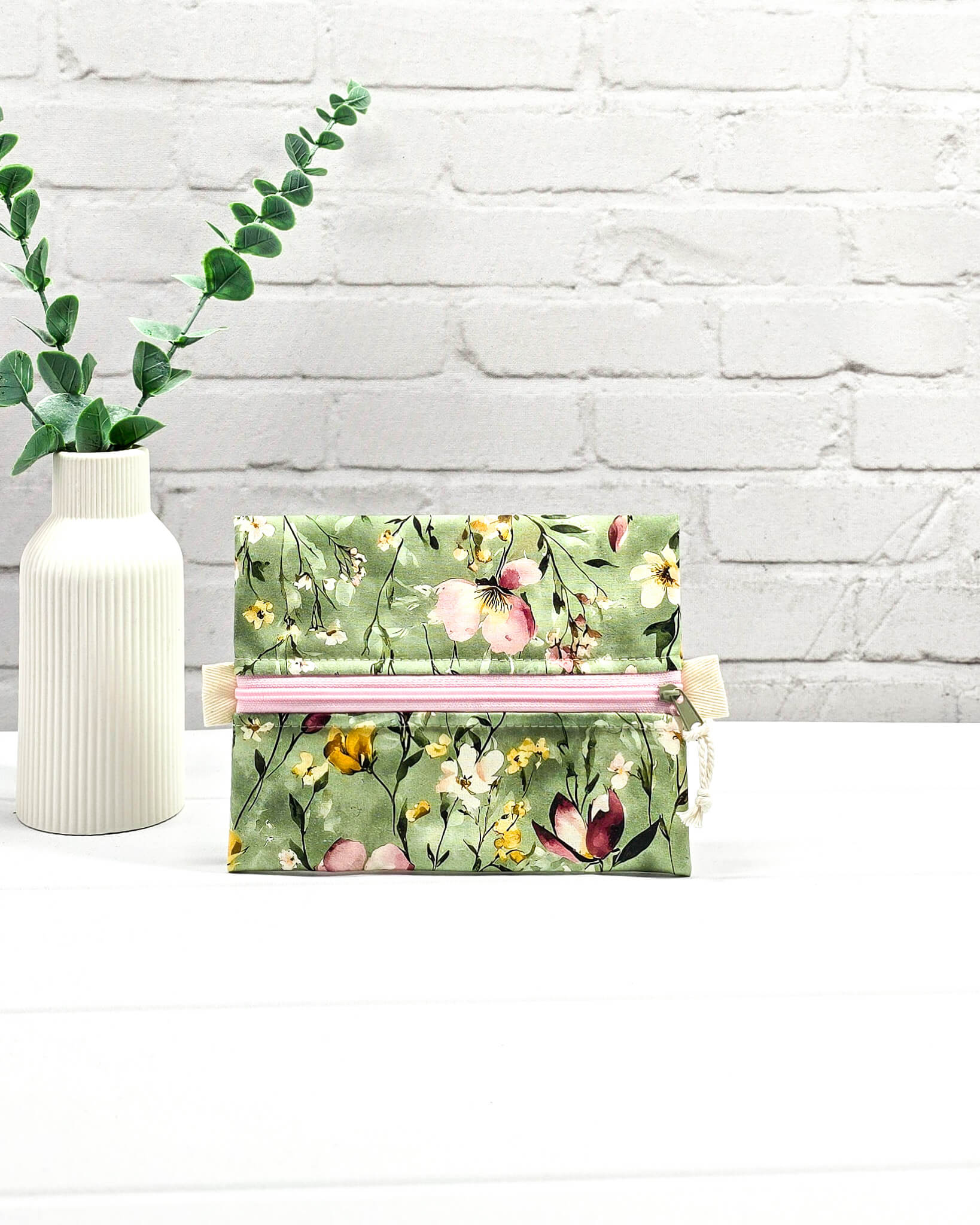 Mini Zip Pouch mit einem floralen Muster auf olivgrünem Stoff, einem rosafarbenen mittigen Reißverschluss und hellen Stofflaschen. Handgenäht in Bayern von Nadelmikado. 