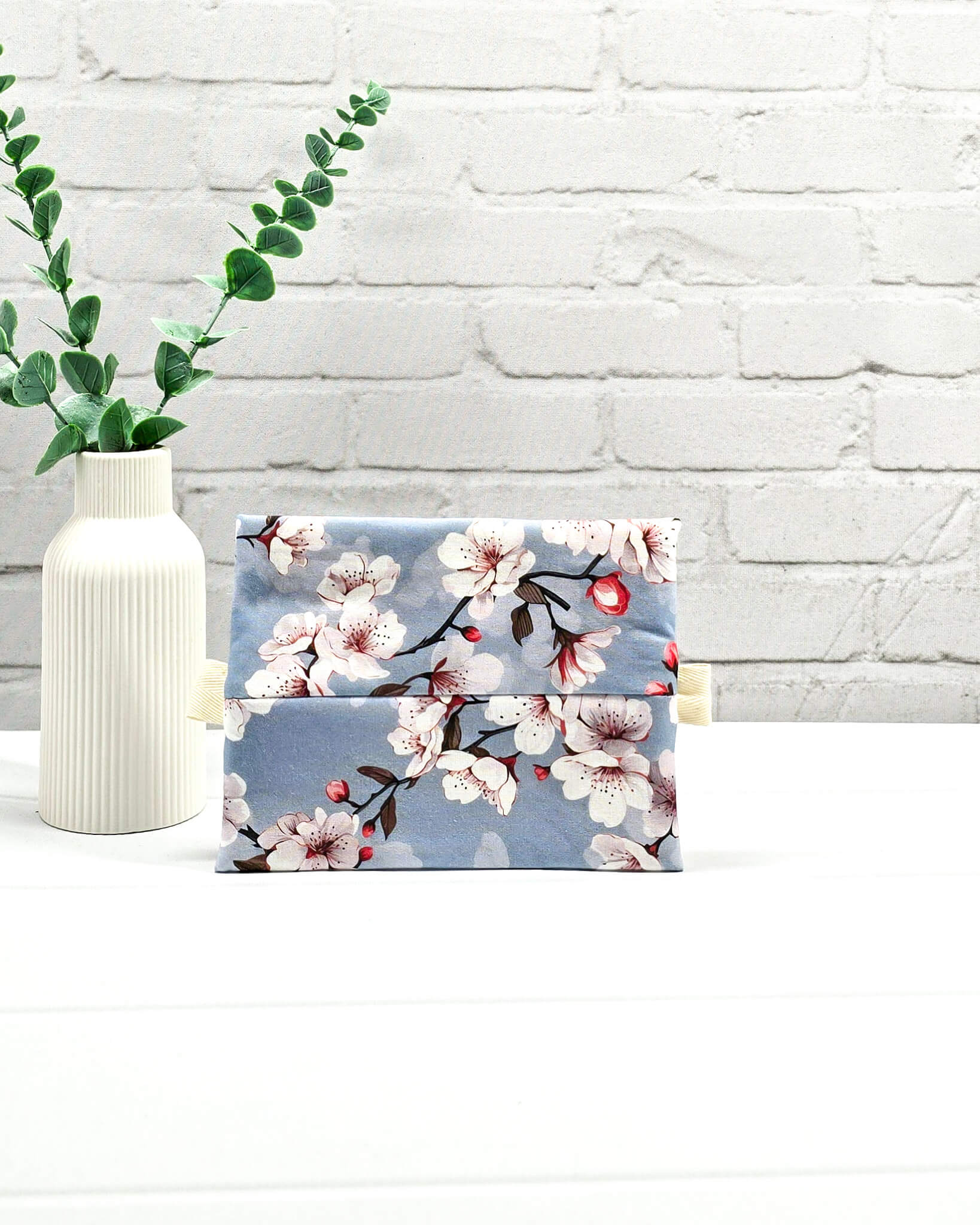 Mini Zip Pouch mit einem Kirschblüten-Muster auf taubenblauem Stoff, einem hellvioletten mittigen Reißverschluss und hellen Stofflaschen. Handgenäht in Bayern von Nadelmikado. 