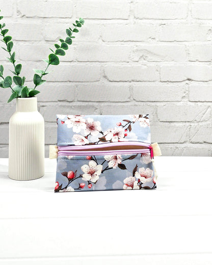 Mini Zip Pouch mit einem Kirschblüten-Muster auf taubenblauem Stoff, einem hellvioletten mittigen Reißverschluss und hellen Stofflaschen. Handgenäht in Bayern von Nadelmikado. 