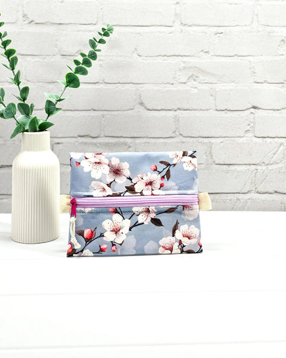 Mini Zip Pouch mit einem Kirschblüten-Muster auf taubenblauem Stoff, einem hellvioletten mittigen Reißverschluss und hellen Stofflaschen. Handgenäht in Bayern von Nadelmikado. 