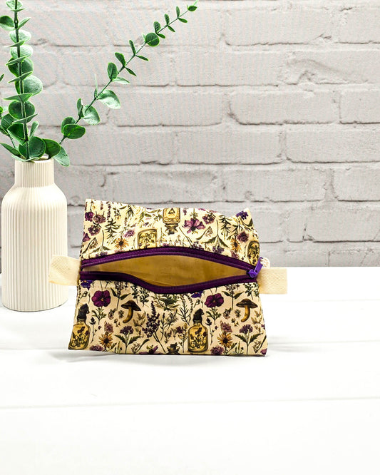 Kleine Reißverschlusstasche Mini Zip Pouch mit lila Reißverschluss, seitlichen hellen Laschen und botanischem Kräuterküche-Muster auf beigem Grund. Handgenäht in Bayern von Nadelmikado.