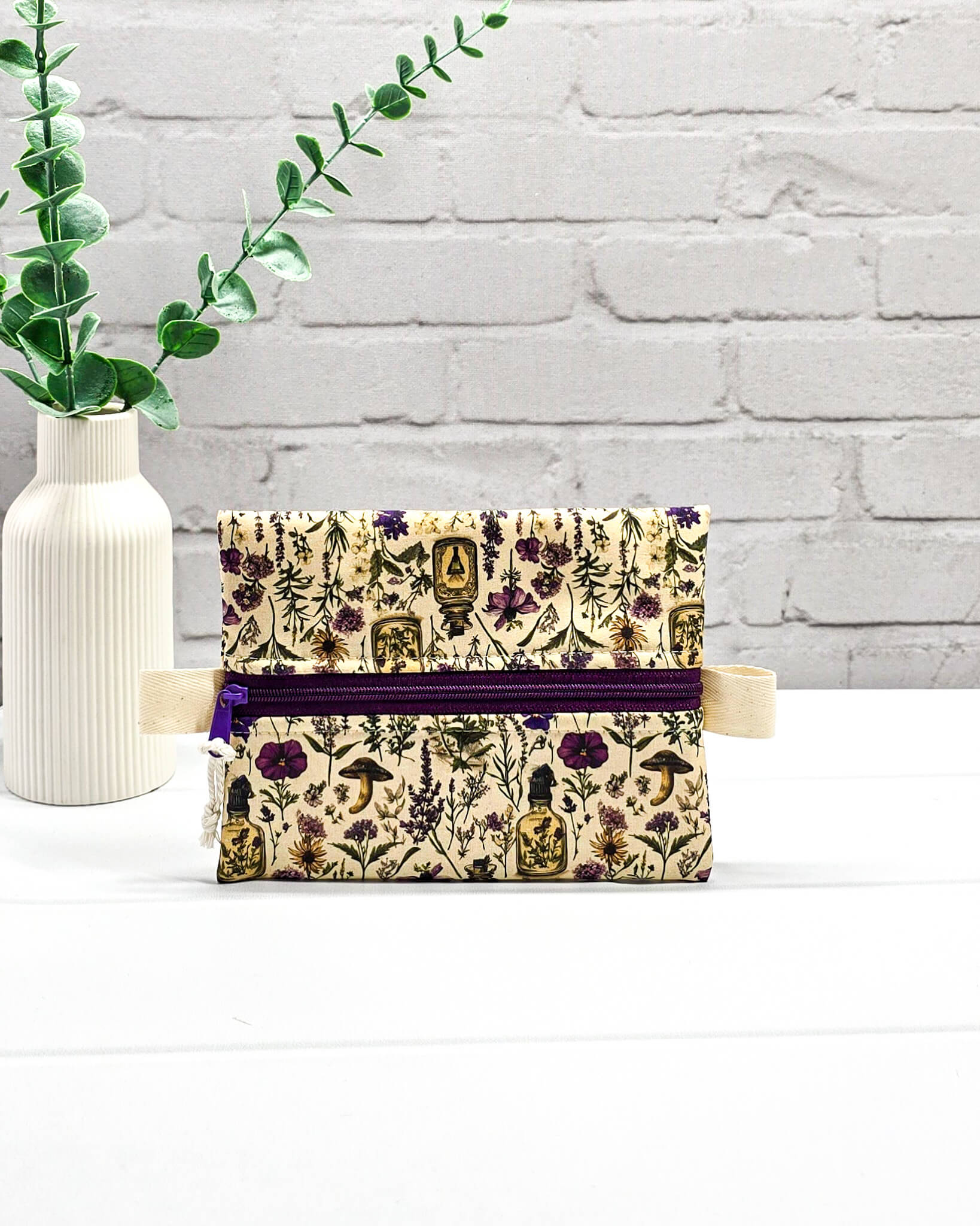Kleine Reißverschlusstasche Mini Zip Pouch mit lila Reißverschluss, seitlichen hellen Laschen und botanischem Kräuterküche-Muster auf beigem Grund. Handgenäht in Bayern von Nadelmikado.
