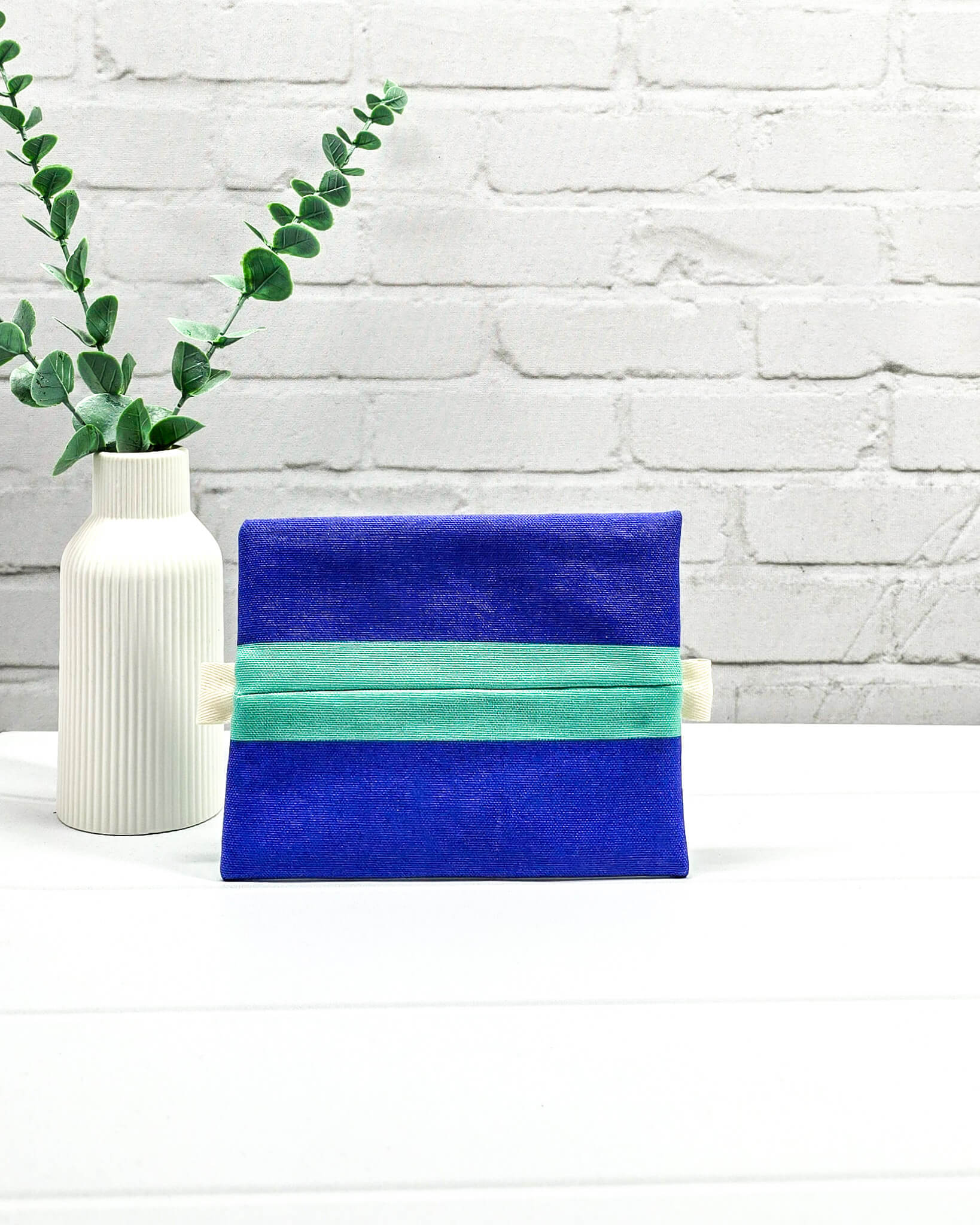 Mini Zip Pouch in Mintgrün mit einem blauen Kontraststreifen, einem schwarzen mittigen Reißverschluss und hellen Stofflaschen. Handgenäht in Bayern von Nadelmikado. 