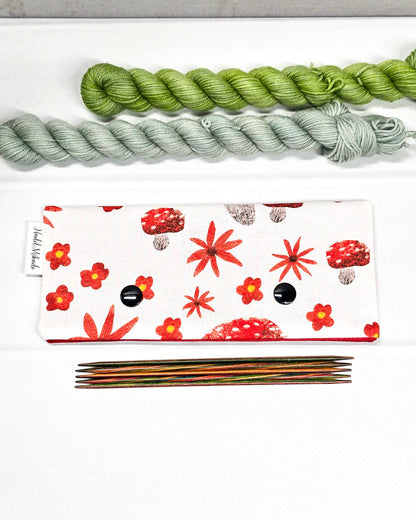 Nadelgarage für 15 cm lange Nadelspiele mit zwei schwarzen Druckknöpfen, roten Fliegenpilzen und herbstlichen Blumenmotiven auf hellem Stoff. Handgenäht in Bayern von Nadelmikado.