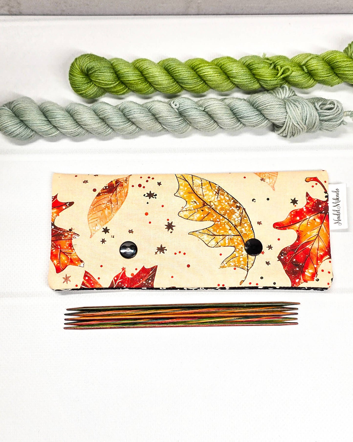 Nadelgarage für 15 cm lange Nadelspiele mit zwei schwarzen Druckknöpfen und herbstlichem Ahornblatt-Muster auf beigefarbenem Grund. Handgenäht in Bayern von Nadelmikado.